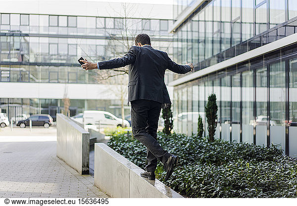 Rear view of businessman balancing on a wall outside office building