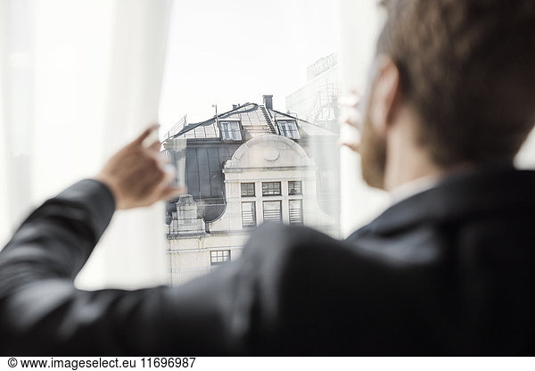 Rear view of businessman looking at building through hotel window
