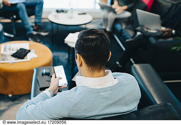 Rear view of businessman using smart phone while working in creative office