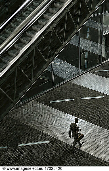 Rear view of businessman walking by escalator on walkway