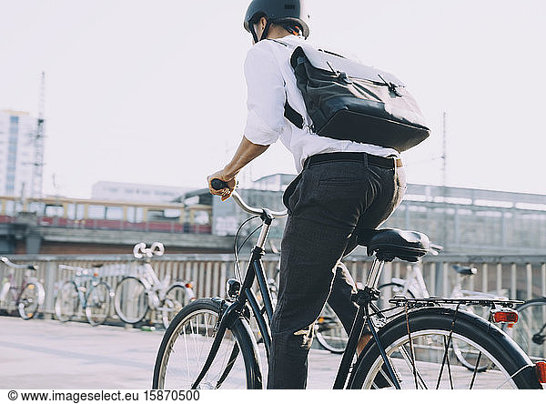 Rear view of businessman with backpack riding bicycle on sidewalk in city