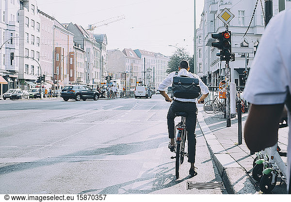 Rear view of businessman with bicycle standing at road signal in city