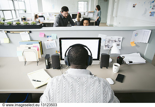 Rear view of businessman working on desktop computer with colleagues in background