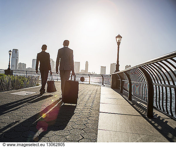 Rear view of businessmen walking with luggage while walking on promenade during sunny day