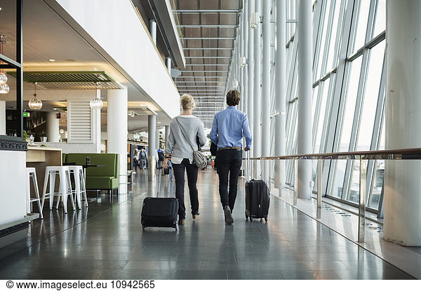 Rear view of businesspeople with luggage walking at airport