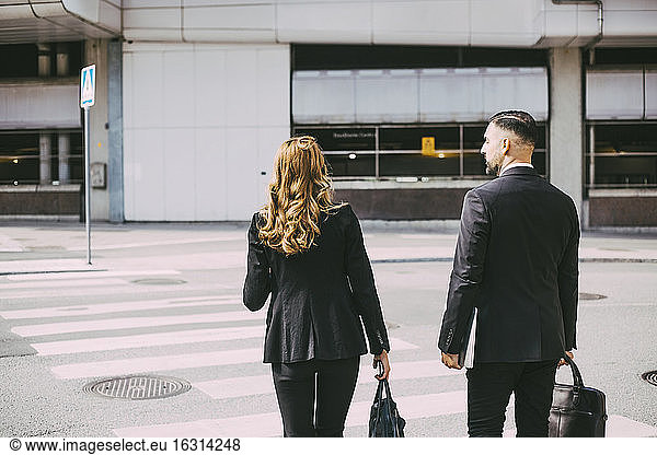 Rear view of businesswoman and businessman crossing road in city
