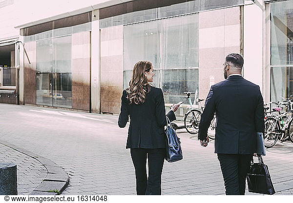 Rear view of businesswoman and businessman walking in city