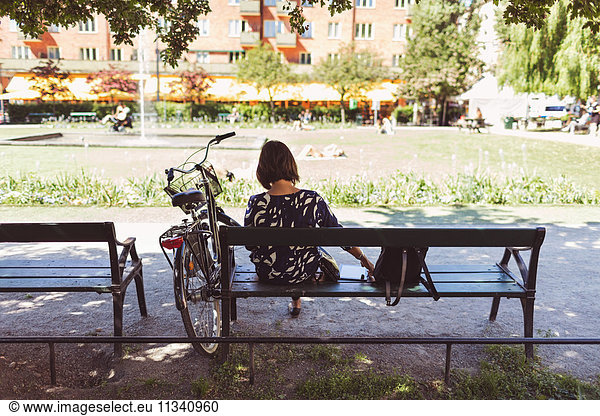 Rear view of businesswoman sitting on park bench by bicycle