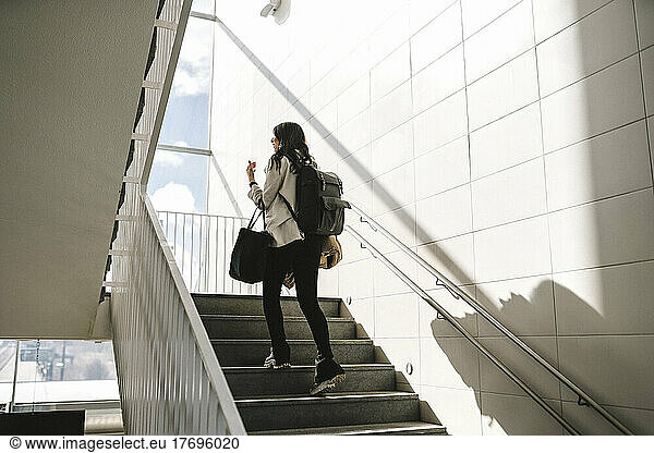 Rear view of businesswoman with backpack moving up on staircase at railroad station