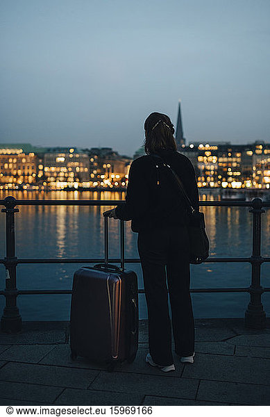 Rear view of businesswoman with luggage looking at illuminated city