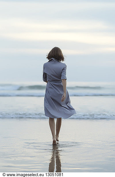 Rear view of carefree woman walking towards sea on shore at beach during sunset, Rear view of carefree woman walking towards sea on shore at beach during sunset
