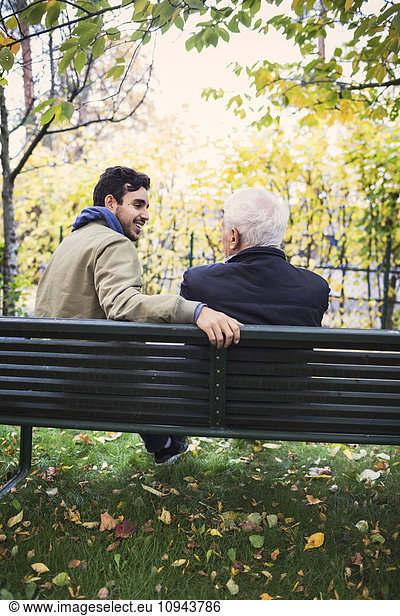 Rear view of caretaker looking at senior man while sitting on bench at park