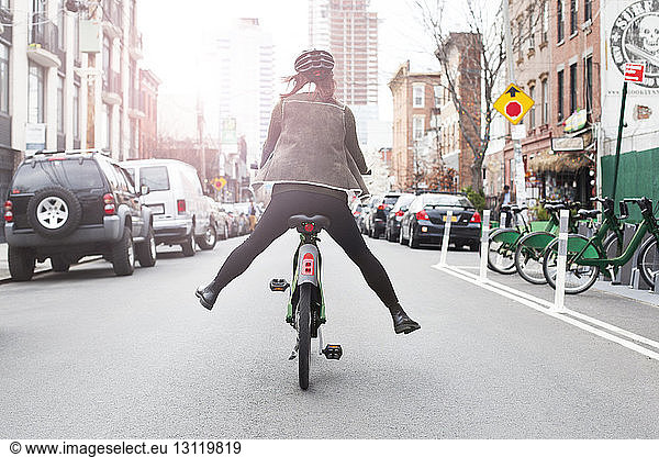 Rear view of cheerful young woman riding bicycle on street
