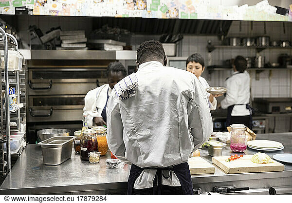 Rear view of chef working with colleagues in kitchen of restaurant