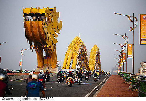 Rear view of commuters on motorcycles crossing bridge in the shape of a dragon.