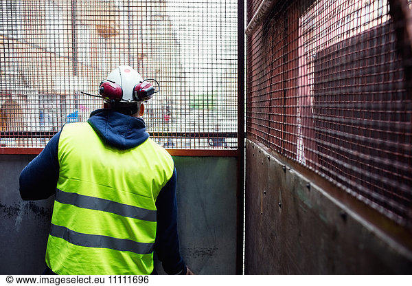 Rear view of construction worker looking through metal grate