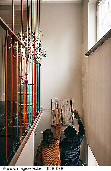 Rear view of couple taking measurement while hanging painting on wall at home