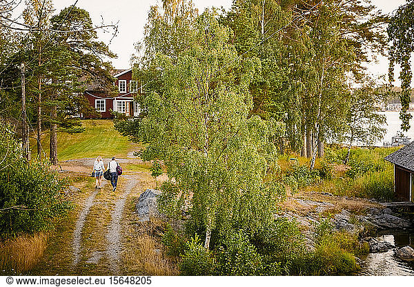 Rear view of couple with luggage walking towards log cabin