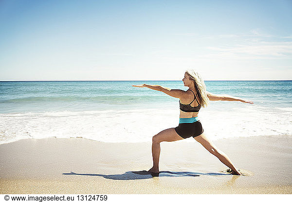 Rear view of determined woman practicing yoga in Warrior 2 pose on Delray beach