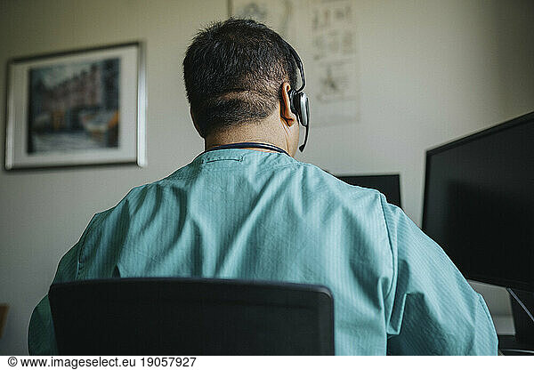 Rear view of doctor wearing headset using computer during online consultation