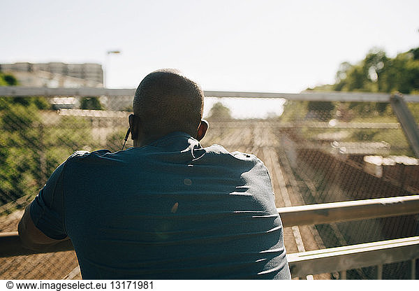 Rear view of exhausted male athlete leaning on railing during sunny day