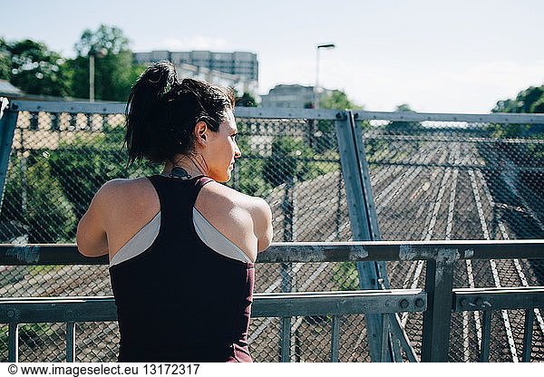 Rear view of exhausted sportswoman leaning on railing at bridge