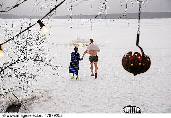 Rear view of father and son holding hands while walking on snow at frozen lake