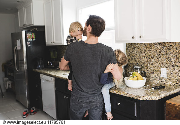 Rear view of father taking care of daughters in kitchen at home