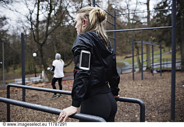 Rear view of female athlete wearing arm band while exercising on parallel bars in forest