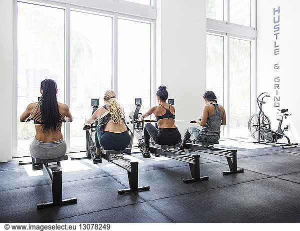 Rear view of female athletes exercising on machines in crossfit gym