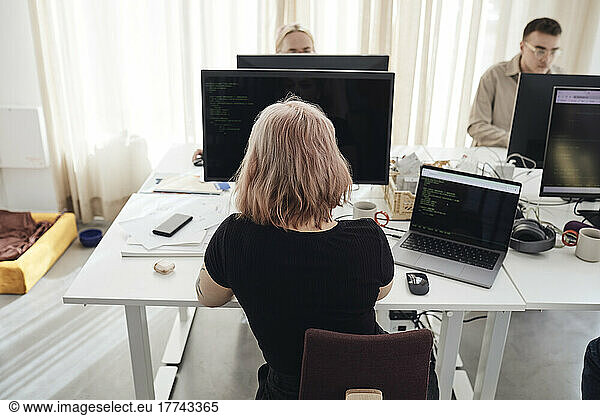 Rear view of female businesswoman working on computer while sitting at desk in office