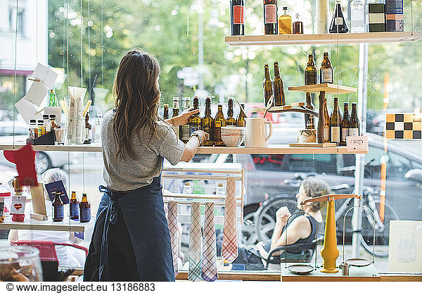 Rear view of female employee arranging bottles on shelf in deli
