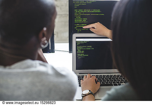Rear view of female entrepreneur pointing at codes on computer monitor to male hacker in office