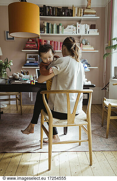 Rear view of female entrepreneur sitting with male toddler on chair at home office
