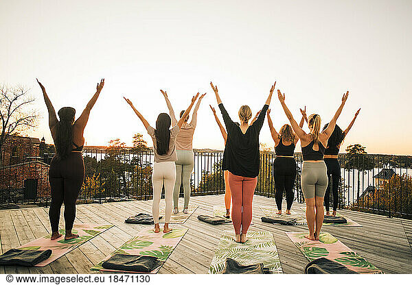 Rear view of female friends exercising with arms raised on patio