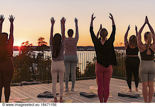 Rear view of female friends standing with arms raised on patio at retreat center