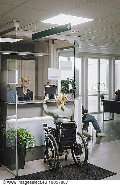 Rear view of female patient with disability doing inquiry at hospital reception
