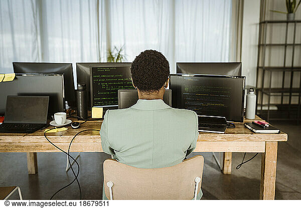 Rear view of female programmer working on computer in creative office