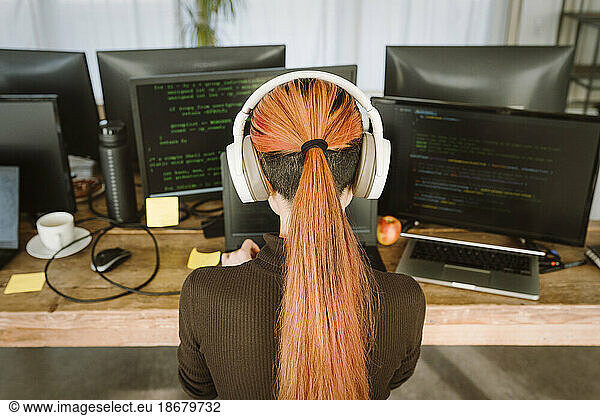 Rear view of female programmer working on laptop in creative office