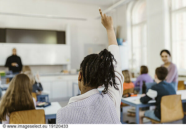 Rear view of female student raising hand during lecture in classroom