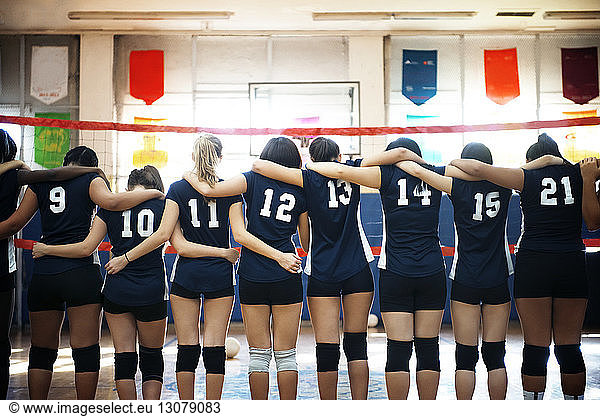 Rear view of female team standing in volleyball court