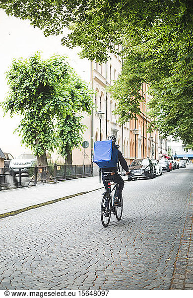 Rear view of food delivery man riding bicycle on street in city