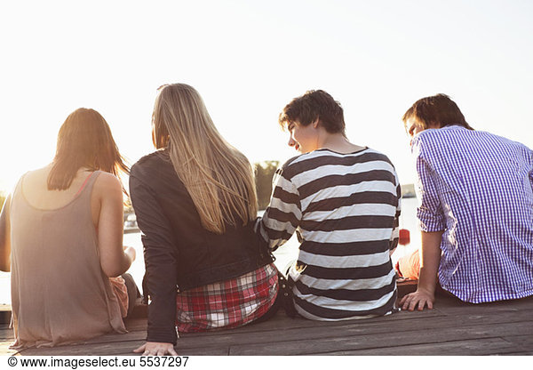 Rear view of four friends sitting on jetty