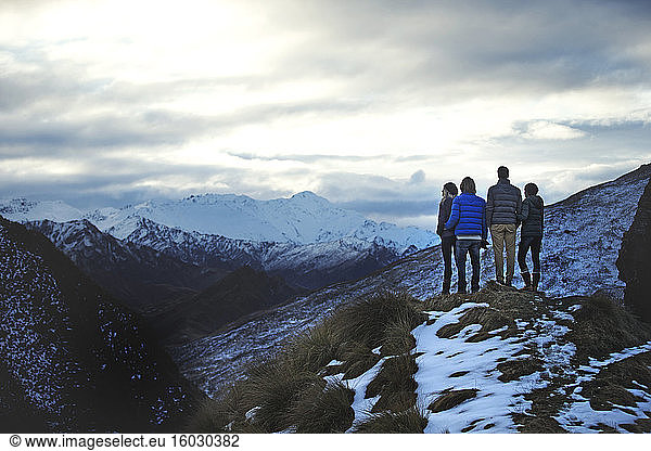 Rear view of four people standing side by side on a mountain  snow-capped peaks in the distance.