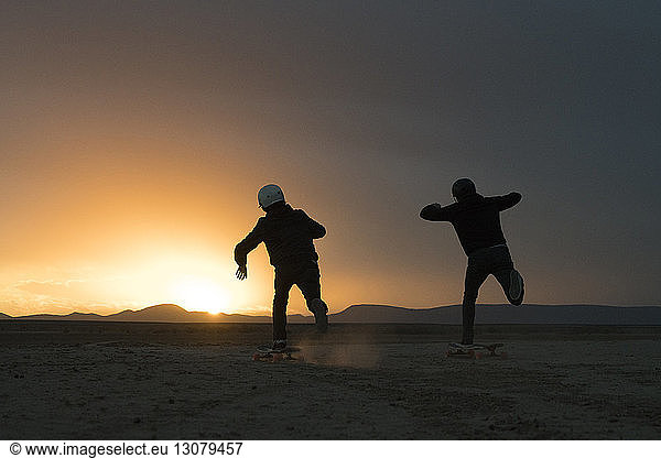Rear view of friends skateboarding against sky during sunset