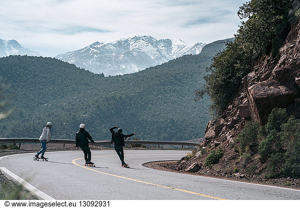 Rear view of friends skateboarding on road against mountain