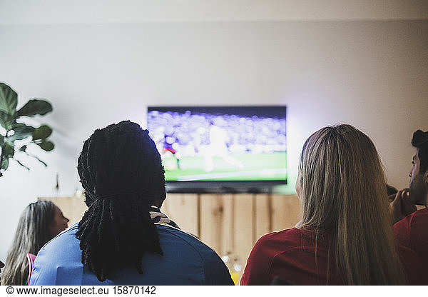 Rear view of friends watching soccer match while sitting at living room
