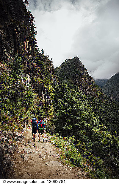 Rear view of friends with backpacks walking at Sagarmatha National Park against cloudy sky