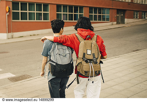 Rear view of friends with backpacks walking on street in city