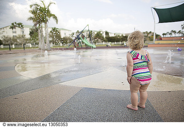 Rear view of girl in swimwear standing by fountain against sky